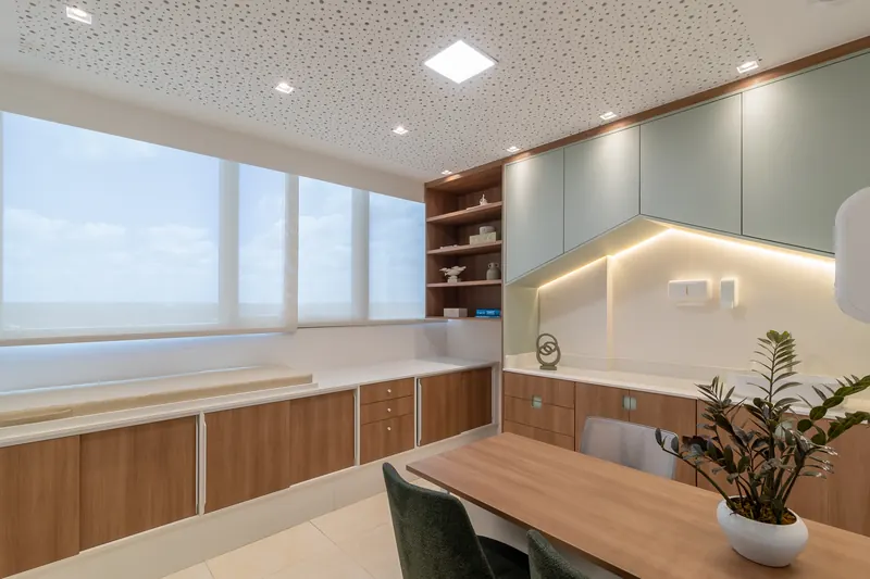 Sala de atendimento com marcenaria em madeira e armários verde-sálvia formando o desenho de uma casinha iluminada.