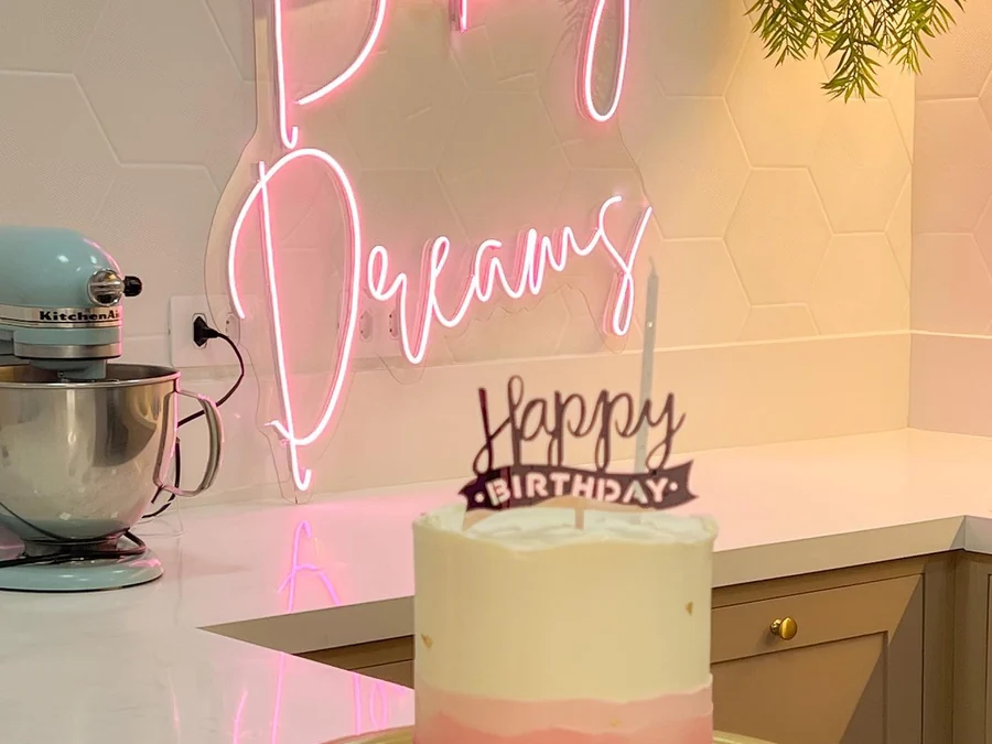 Sala de cursos com letreiro de neon rosa, revestimento hexagonal e batedeira sobre a bancada.