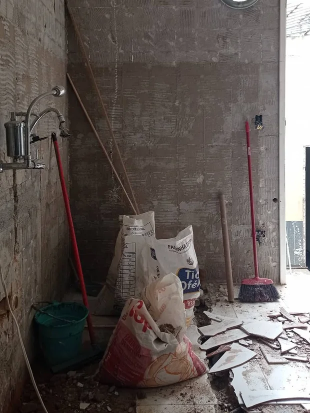 Parede demolida com sacos de material e revestimento retirado no chão.