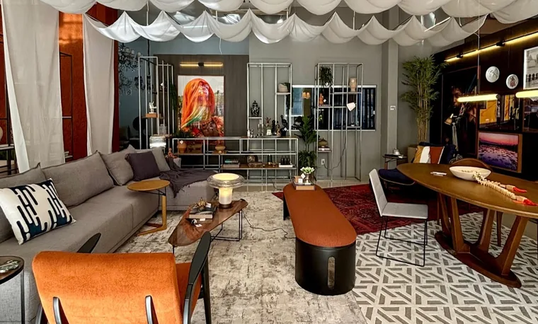 Estar do Espaço do Colecionador com forro de tecido drapeado, poltrona laranja e mesa de jantar.