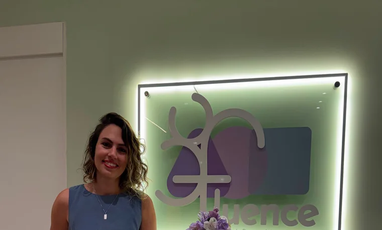 Espera da Clínica Fluence, com o letreiro branco sobre a parede roxa e prateleiras de livros infantis.