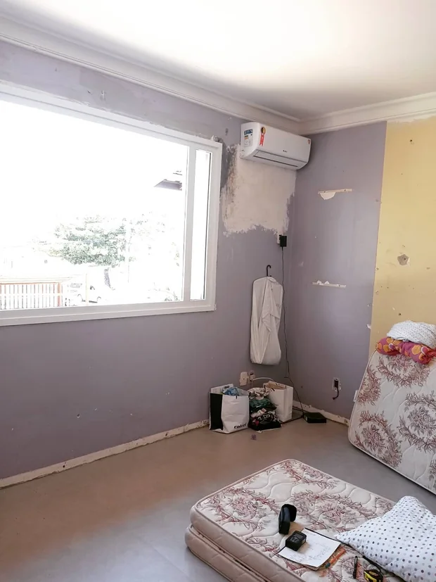 Quarto antes da reforma, com parede lilás, móveis soltos e piso em obra.